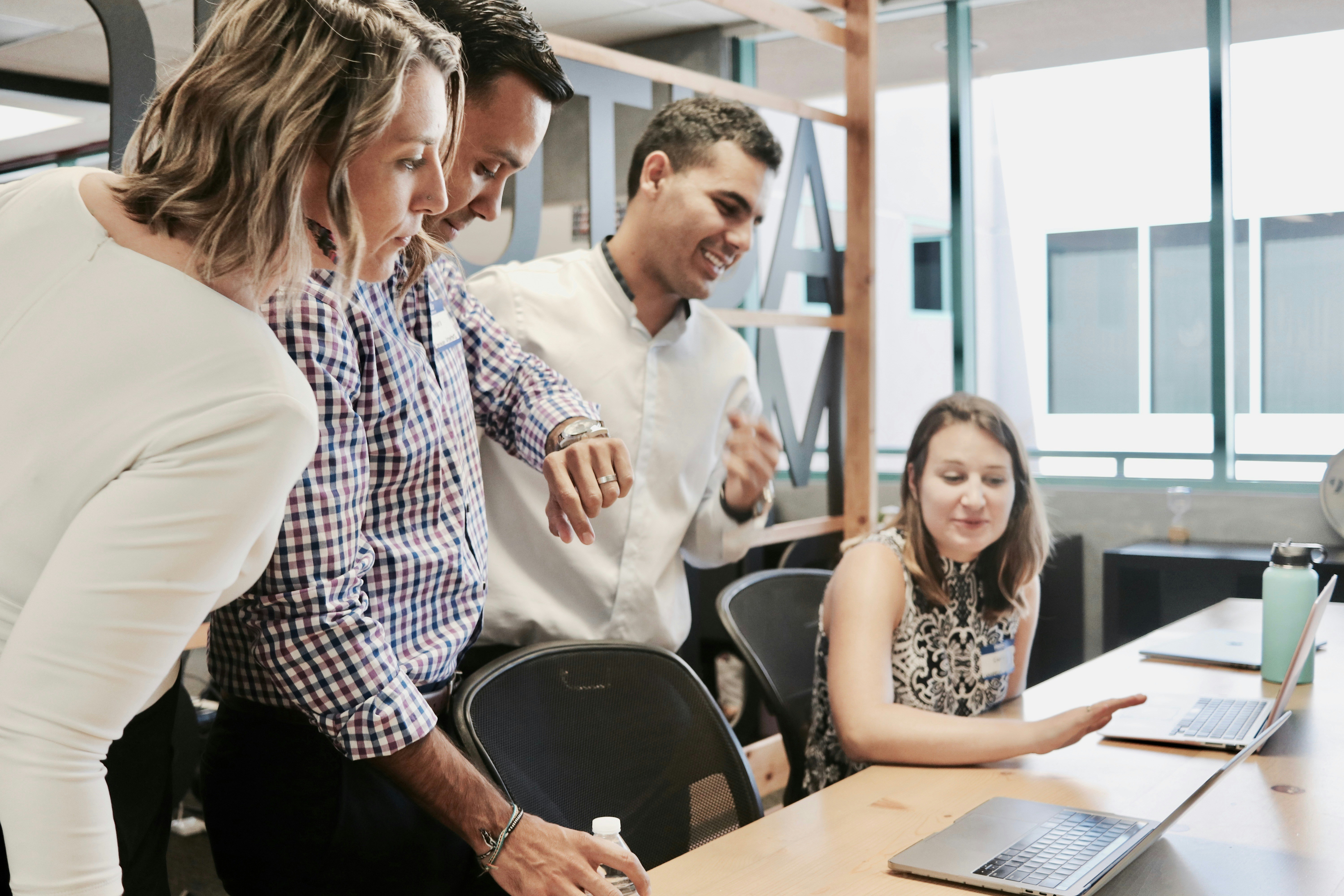 A diverse group of individuals gathered around a laptop, engaged in discussion and collaboration.